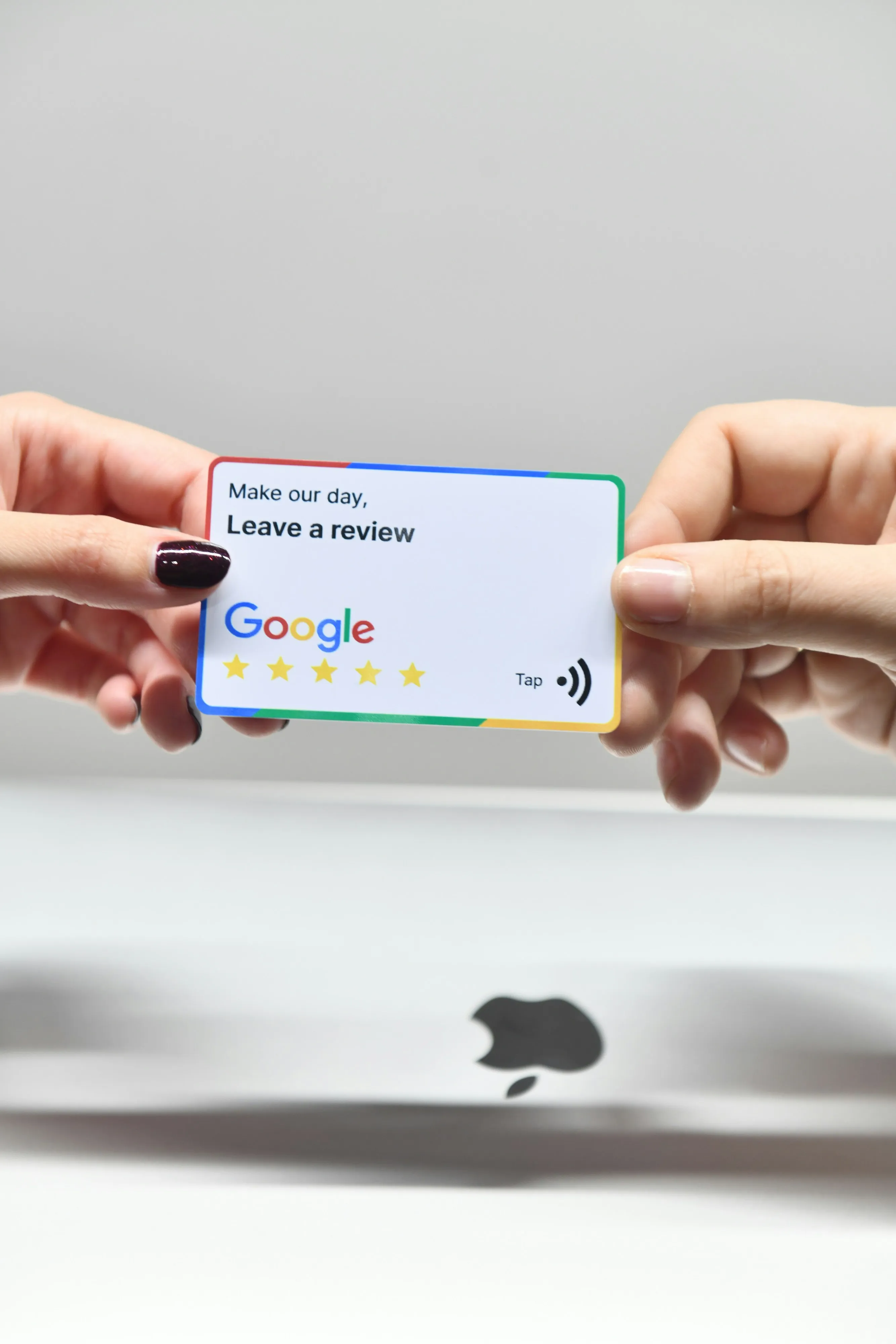 Two hands hold an NFC "Leave a review" card with the Google logo and five stars, next to a laptop.
